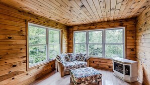 A cabin with wooden walls and floors, a sofa, an ottoman, and a fireplace. - Cozy Cabin on the River  (Topton)