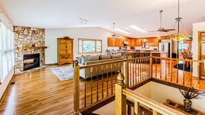 A spacious living area with a stone fireplace, wooden furniture, and a view of the kitchen and dining area. - Cozy Cabin on the River  (Topton)
