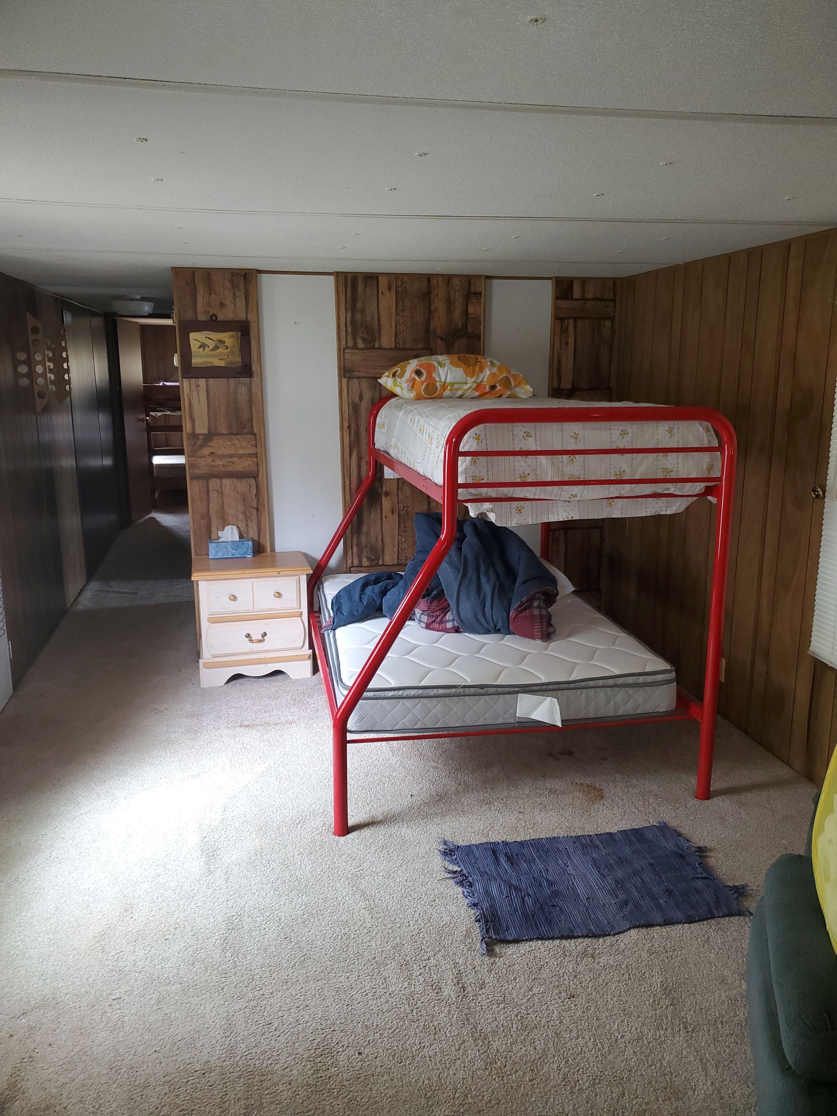 Una cama individual con estructura roja, un armario de madera, un pequeño aparador y una alfombra azul.