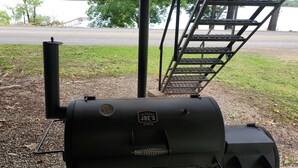 Una parrilla exterior negra con rejilla metálica, una chimenea y una etiqueta que dice "Oklahoma Jobs Smokes".