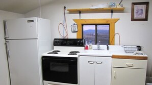 Eine kompakte Küche mit Kühlschrank, Herd, Backofen und Spüle mit Fenster darüber.