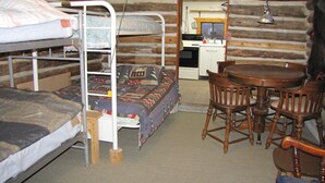 Ein Holzblockhaus-Interieur mit Stockbetten, einem Holztisch und einer Küchenzeile.