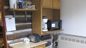 Eine kompakte Küche mit Holzschränken, einer Mikrowelle, einer Kaffeemaschine und einem kleinen Kühlschrank.