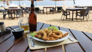 Ein Esstisch direkt am Strand mit einem Teller frittiertem Essen, einer Bierflasche und einem Bierglas.