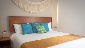 Ein ordentlich bezogenes Bett mit Holz-Kopfteil, weißer Bettwäsche und goldener Tagesdecke.