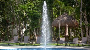 Ein Pool mit einer zentralen Fontäne, umgeben von Liegestühlen und Palmen.