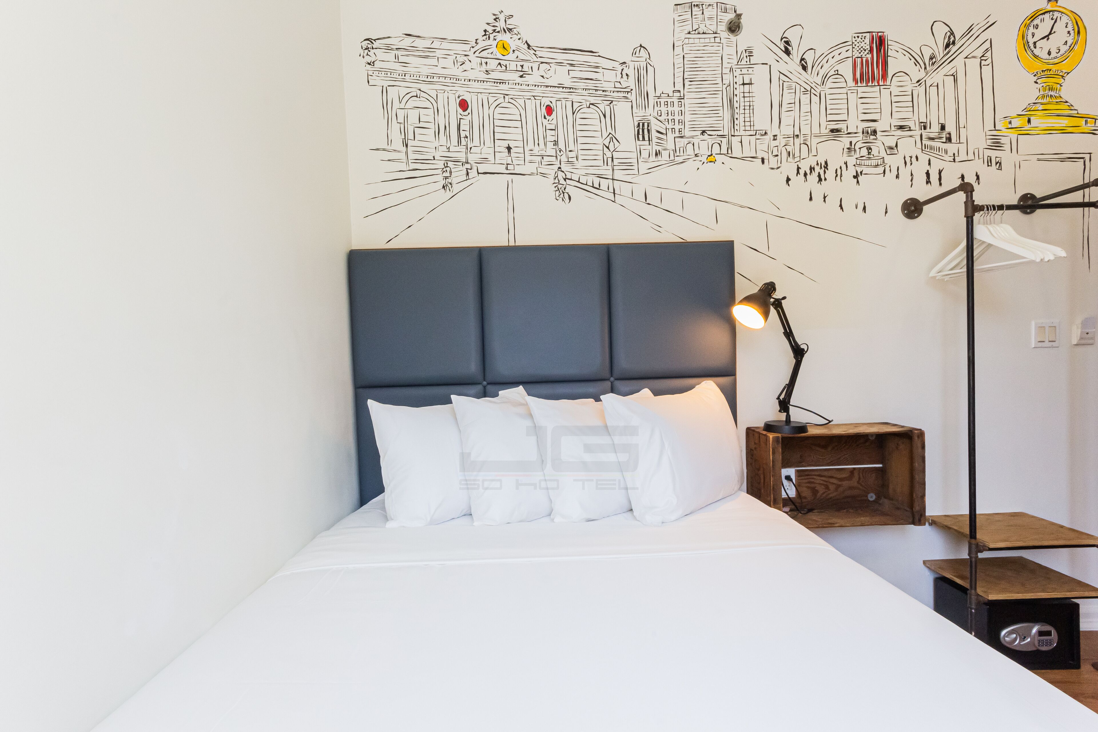 A bed with a dark headboard, white bedding, and a wall mural depicting a city scene.