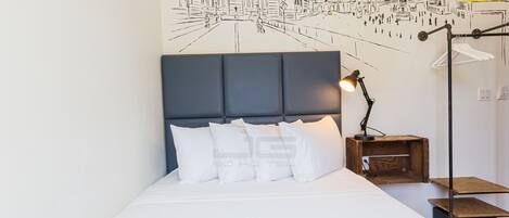 A bed with a dark headboard, white bedding, and a wall mural depicting a city scene.