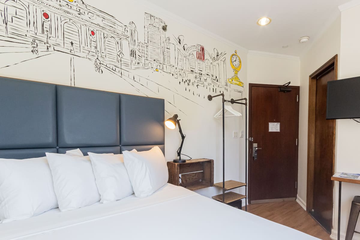 A hotel room with a large bed, a desk, a chair, a TV, and a wall mural.