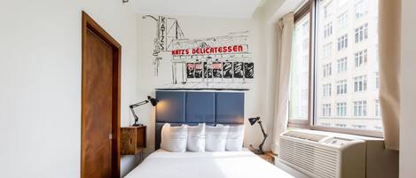 A hotel room with a bed, a headboard, a wall mural, a window, and a radiator.