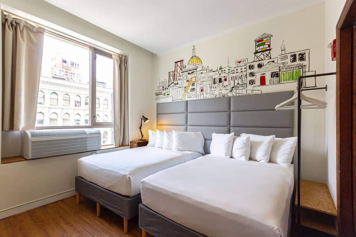 A hotel room with two beds, a large window with curtains, an air conditioning unit, and a cityscape mural on the wall.