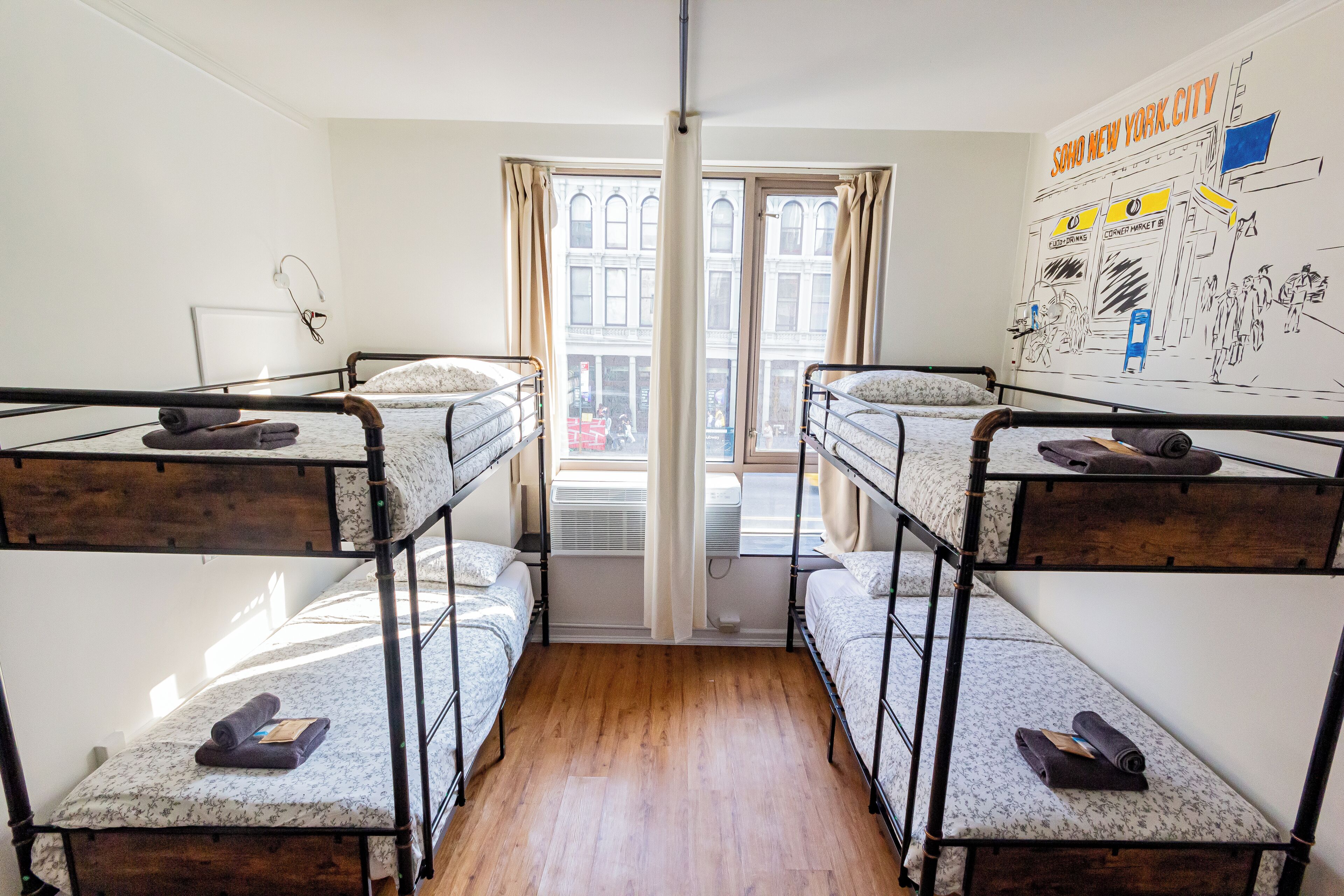 A dormitory room with bunk beds, a window with curtains, and a wall mural.