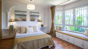 Un dormitorio con una cama grande, un rincón con asiento junto a la ventana y obras de arte en las paredes.