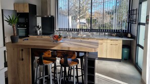 Eine moderne Küche mit einer zentralen Kochinsel, Barhocker und einem großen Fenster mit Blick auf Bäume.