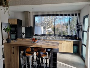 Een moderne keuken met een centraal eiland, barkrukken en een groot raam met uitzicht op bomen.
