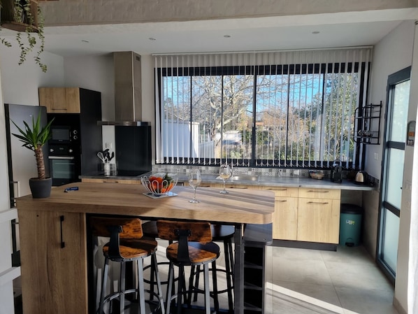 A modern kitchen with a central island, bar stools, and a large window with a view of trees.