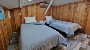 Ein Zimmer mit zwei Betten, Holzwänden, einem Oberlicht und einem kleinen Gemälde.