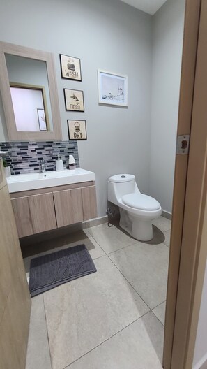 Uma casa de banho moderna com lavatório branco, armários de madeira, sanita e chão em azulejos.