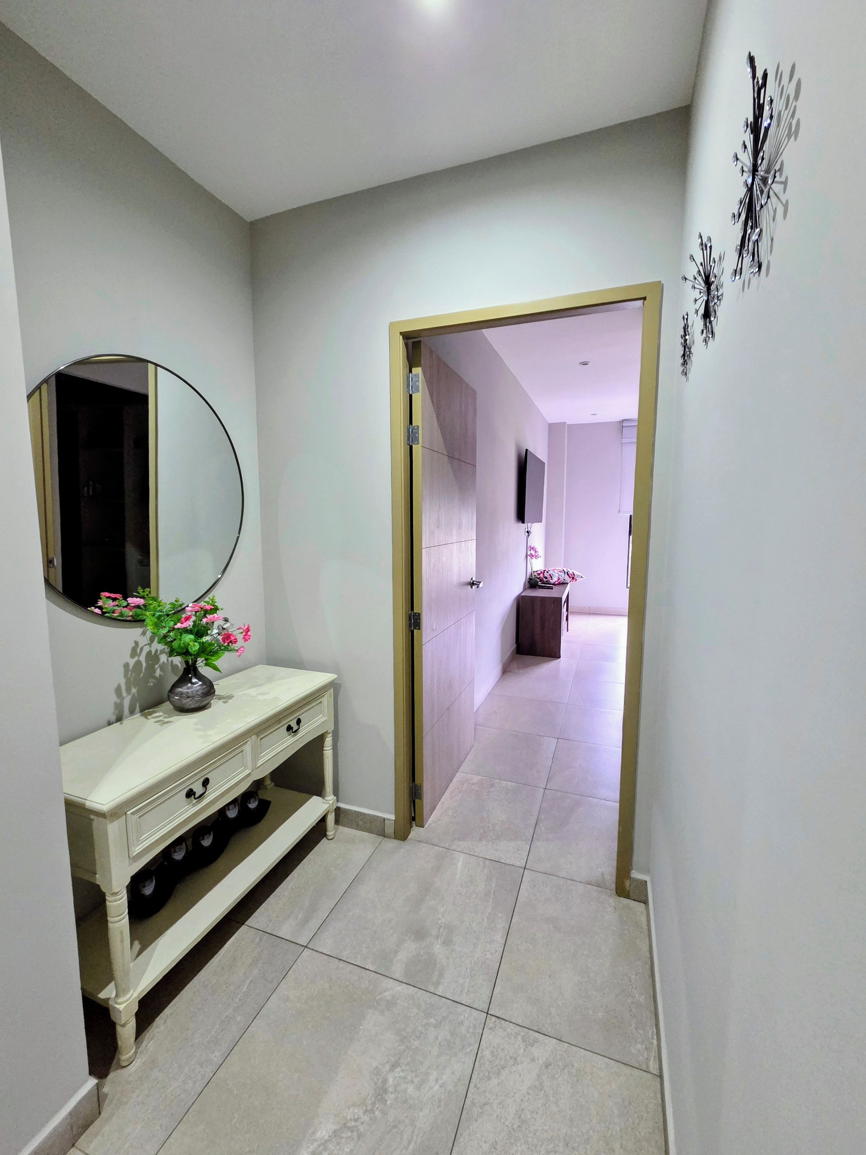 A hallway with a vanity, a mirror, and a door leading to another room.