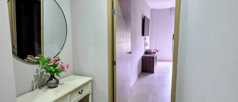 A hallway with a vanity, a mirror, and a door leading to another room.