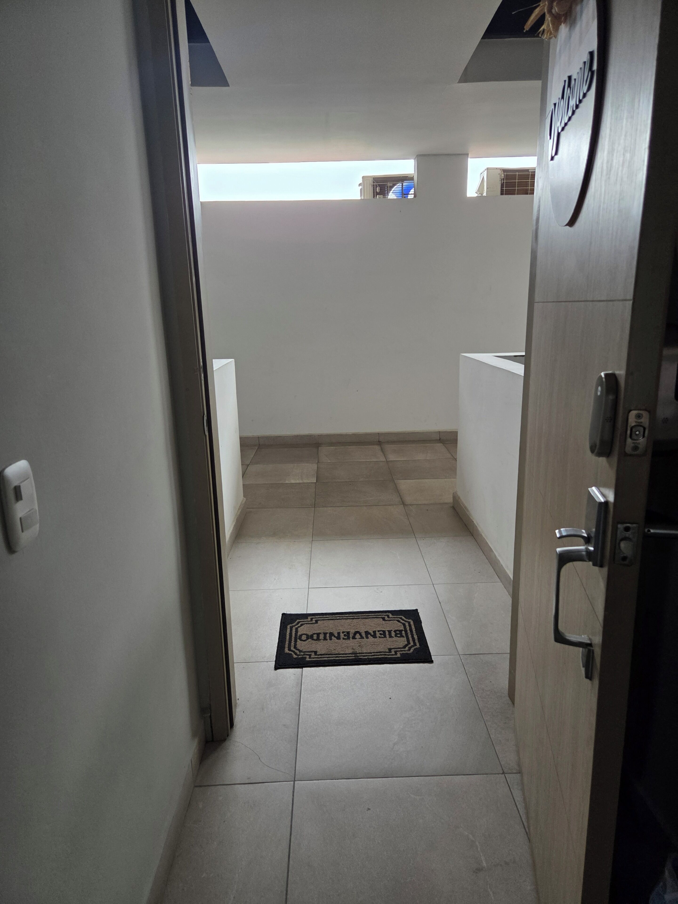 Un pasillo con un felpudo, una puerta con manija y vistas a una habitación con ventana.