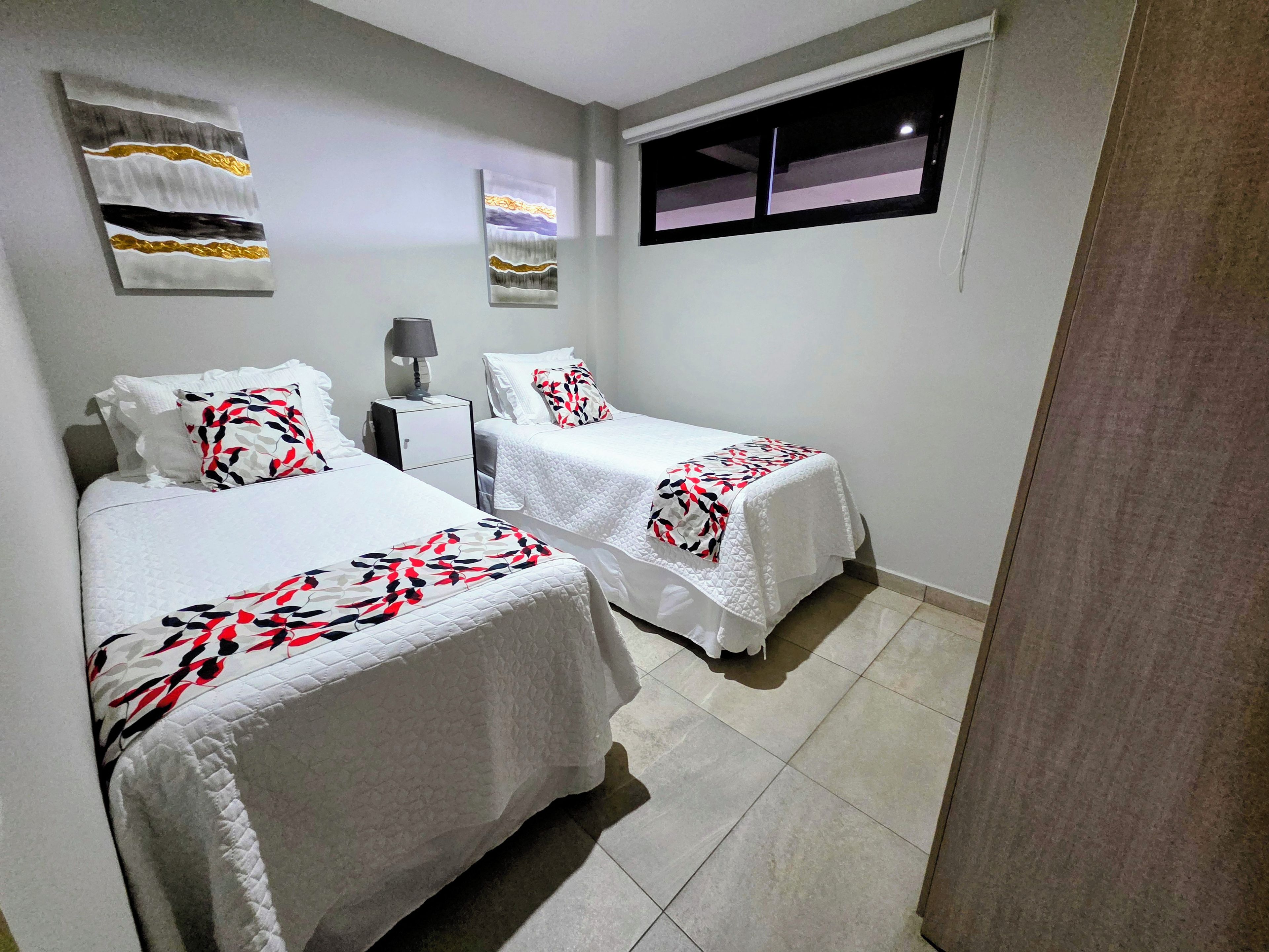 Habitación de hotel con dos camas, una mesita de noche, una lámpara y obras de arte en las paredes.