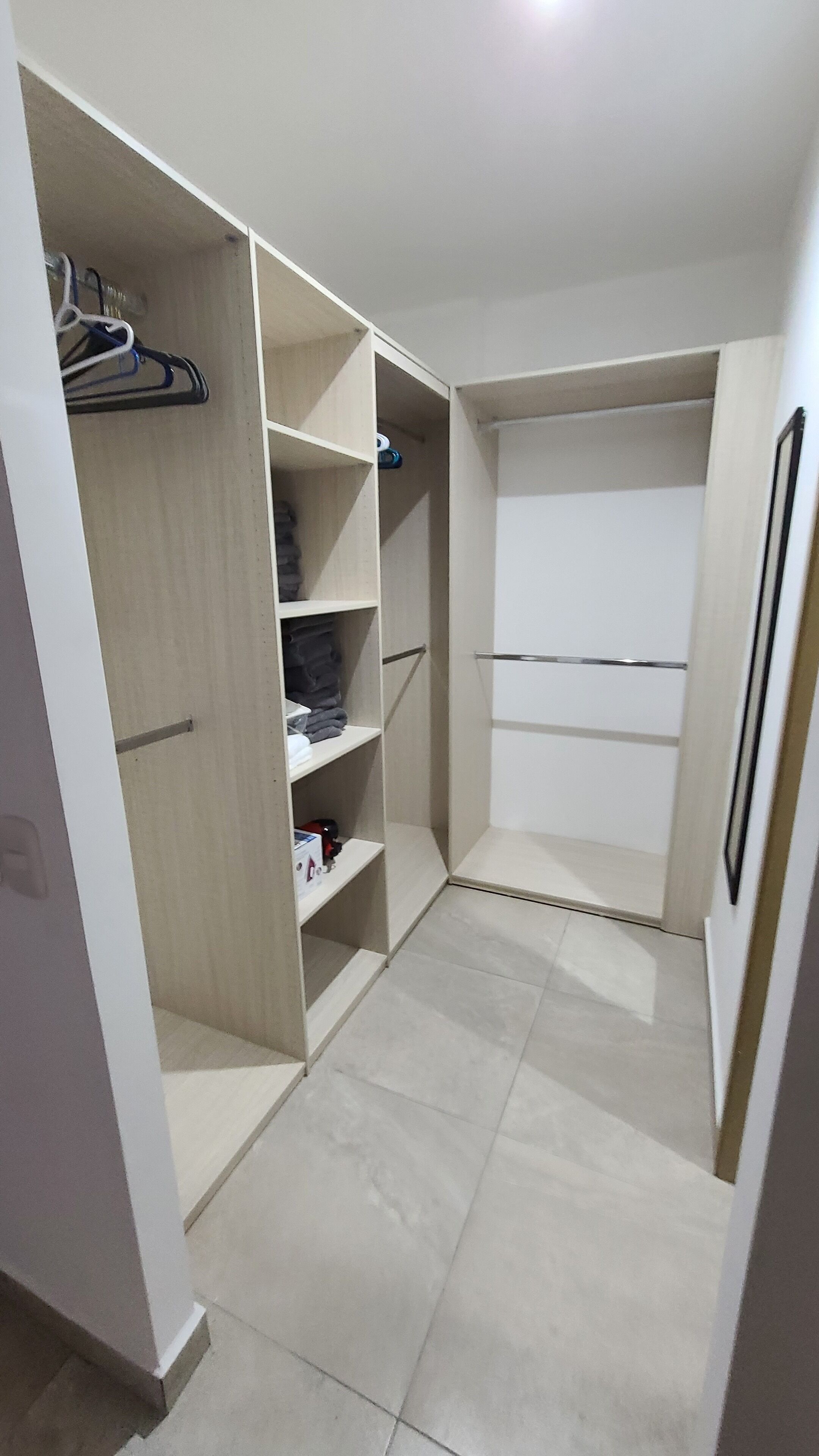 A walk-in closet with multiple shelves and hanging space, light-colored tiles, and a plain white door.