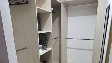 A walk-in closet with multiple shelves and hanging space, light-colored tiles, and a plain white door.