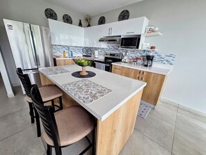 Une cuisine moderne avec des meubles blancs, un réfrigérateur en acier inoxydable, un four à micro-ondes et un coin café.
