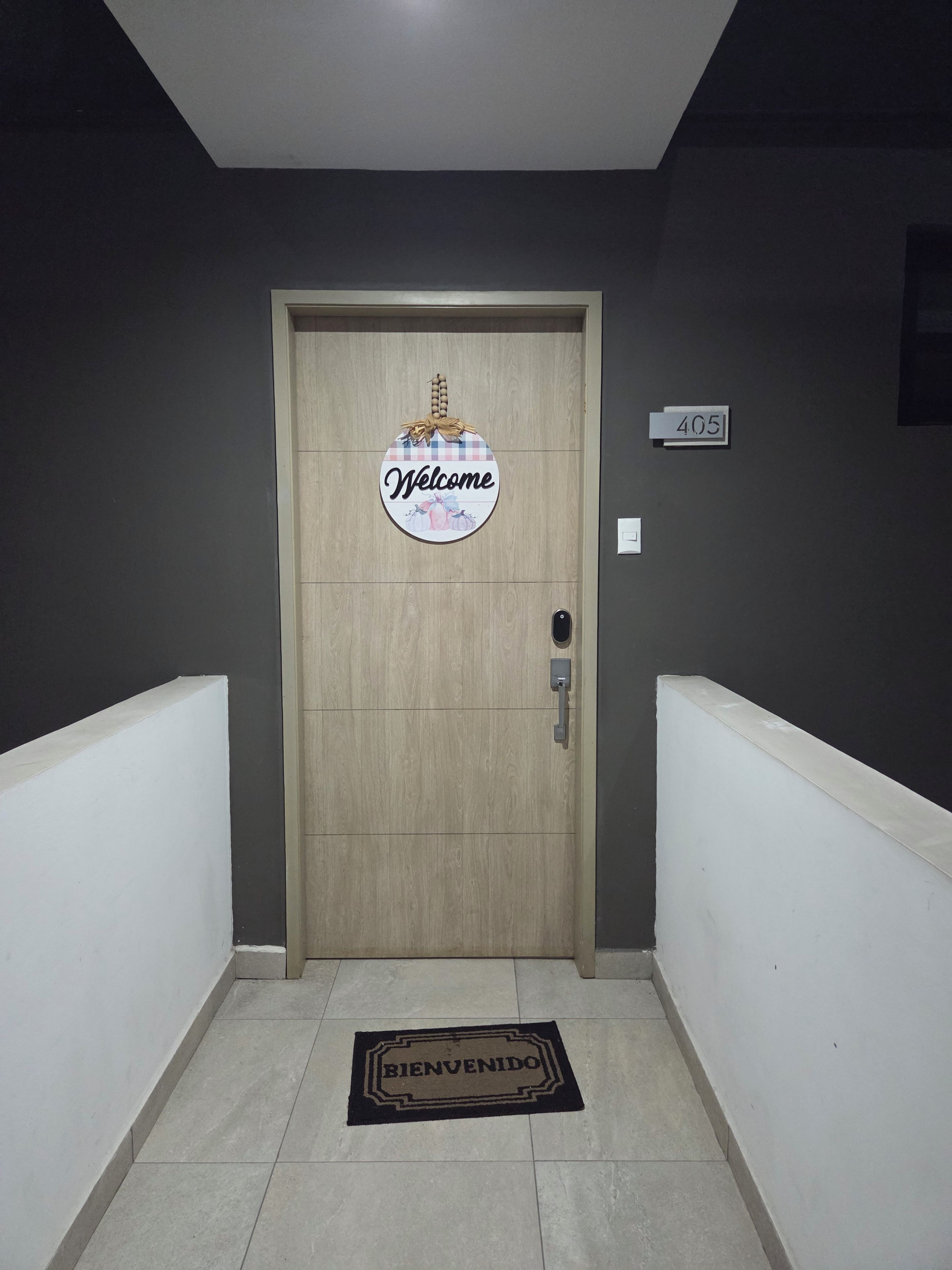 Una puerta con un cartel de 'Welcome', un letrero con el número de la habitación y un felpudo.