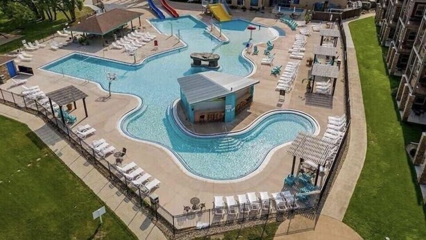 A large swimming pool with multiple slides and a separate pool area, surrounded by lounge chairs and a building with a flat roof. - Luxurious Lakefront  BB Corner Condo.
Panoramic lake views & 6 waterpark passes. (Arnolds Park)