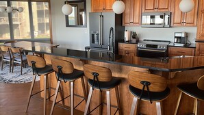 A modern kitchen with wooden cabinets, a central island with bar stools, stainless steel appliances, and pendant lighting. - Luxurious Lakefront  BB Corner Condo.
Panoramic lake views & 6 waterpark passes. (Arnolds Park)