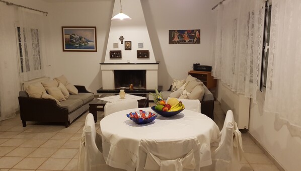 A cozy living room with a fireplace, a dining table with a fruit bowl, and a sofa. - Silver Villa Raches, Sky, next to the Sea. (Raches, Fthotida)