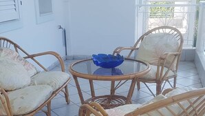 Ein Balkon mit Korbmöbeln, darunter zwei Stühle und ein runder Tisch mit einer blauen Schüssel.