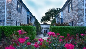 Un bâtiment à la façade en briques, avec les numéros « 213-220 » sur le côté, et un jardin bien entretenu, agrémenté de fleurs roses au premier plan.