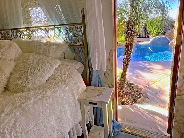 A bedroom with a bed covered in white fluffy bedding, a bedside table, and a view of a pool outside. - Private Oasis Gorgeous Pool, Lush Gardens in the Senoran Preserve, Cave Creek (Phoenix)
