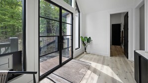 Une pièce spacieuse avec de grandes fenêtres, un plancher en bois et une vue sur une terrasse et des arbres.