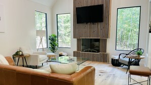 Un salon moderne avec un canapé en cuir, une table basse en verre et une cheminée ornée d’un panneau en bois vertical.