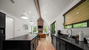 Une cuisine moderne avec des plans de travail noirs, un revêtement de sol en bois et des luminaires suspendus.