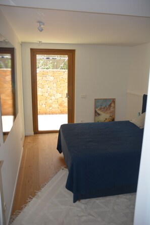 A bedroom with a bed, a door leading to a balcony, a painting on the wall, and a white rug.