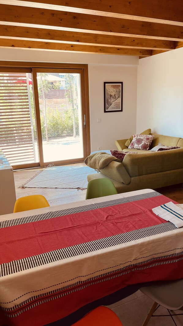 A room with a bed, a sofa, a table, and a sliding glass door leading to an outdoor area.