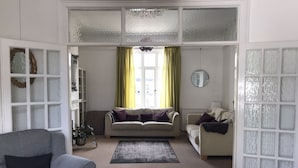 Un salon spacieux avec une grande fenêtre, un canapé, un fauteuil et un miroir décoratif.