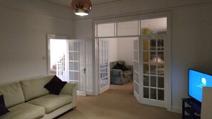 Un salon avec un canapé beige, un téléviseur et une porte donnant sur une autre pièce.