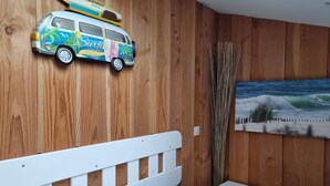 Une chambre avec un mur en bois, un lit doté d’une tête de lit blanche, une petite table de chevet et une décoration murale représentant une planche de surf.