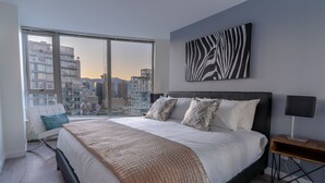 Un dormitori modern amb un llit gran, una vista a la ciutat i una obra d'art amb estampat de zebra.