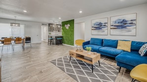 A modern living room with a blue sofa, wooden coffee table, and a dining area with a wooden table and chairs. - West Side 5 bedroom Home. Great Location !!! (El Paso)