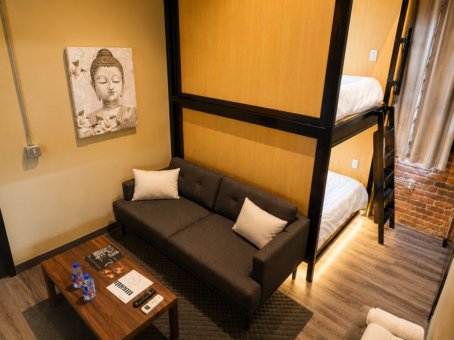 A compact room with a sofa, a small table with items, a bunk bed, and a wall-mounted artwork.