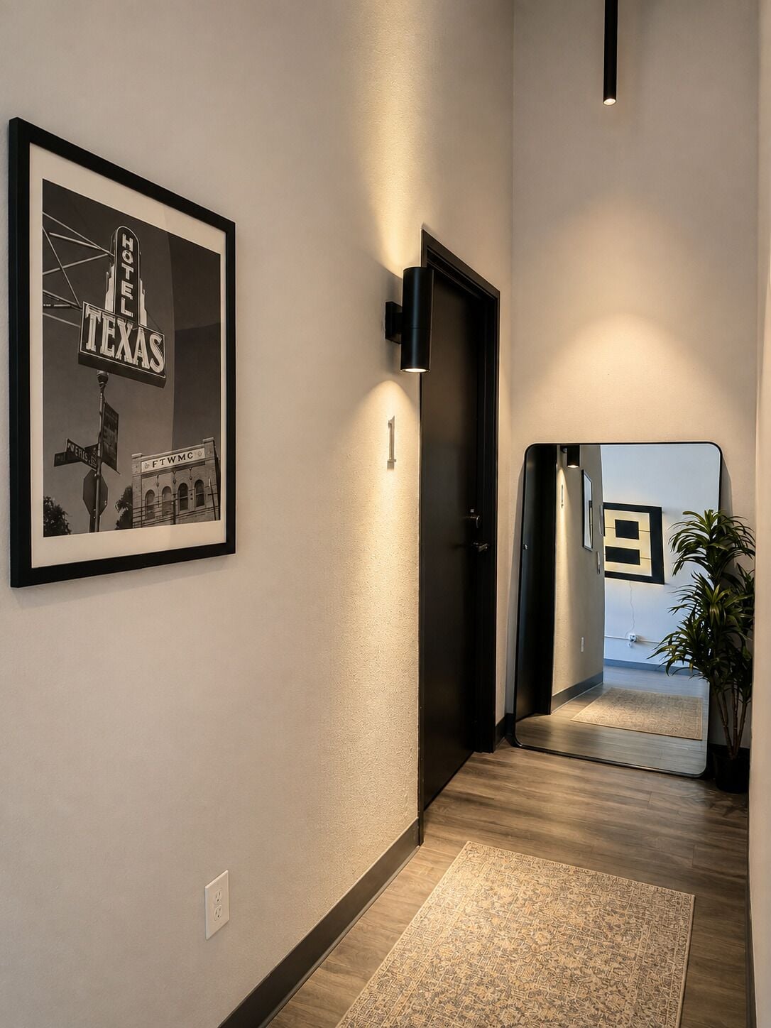 A hallway with a framed sign, a door, a mirror, and a plant.