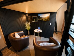A corner room with two leather armchairs, a small round table with a magazine and water bottles, a potted plant, and a wall-mounted picture. - Boxstel - Moderns Stay Hotel (El Paso)
