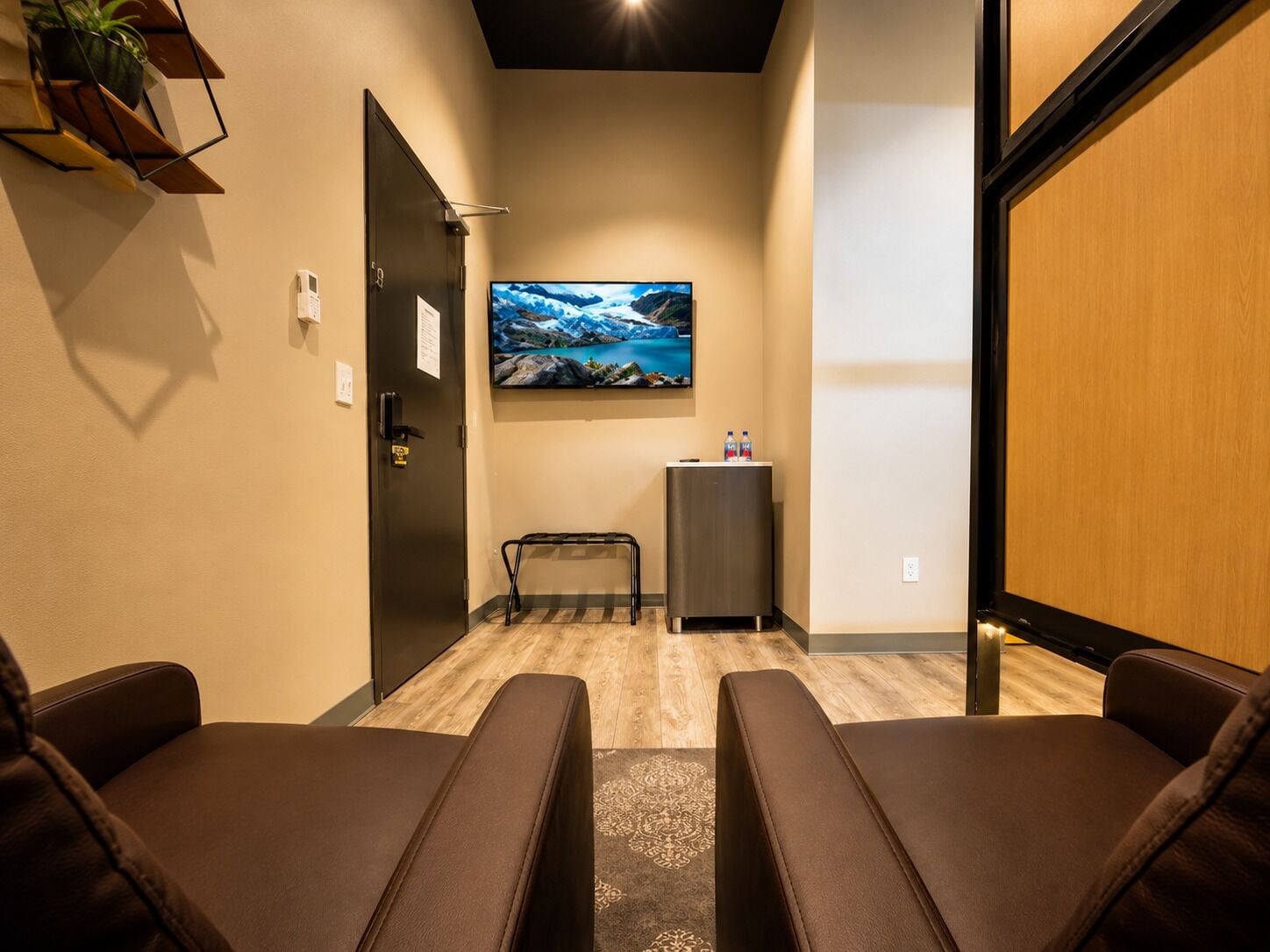 A room with a seating area, a television mounted on the wall, and a small table with water bottles.